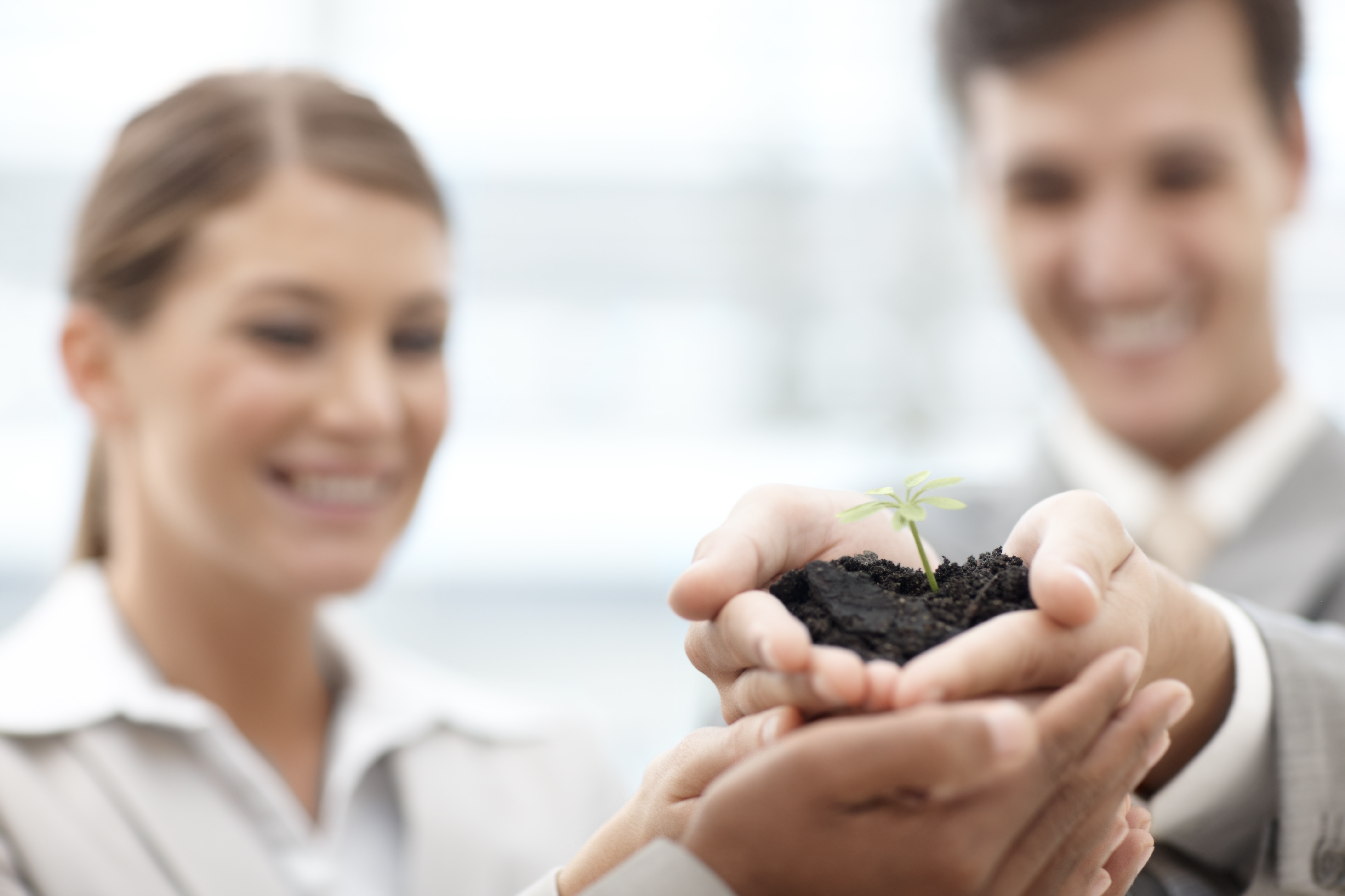 Two colleagues smiling as they hold a sprouting seedling in cupped hands